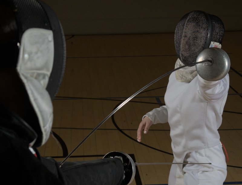 Dieses Foto zeigt eine Schülerin,- die mit einem Degen auf den Arm ihres Trainers stößt.